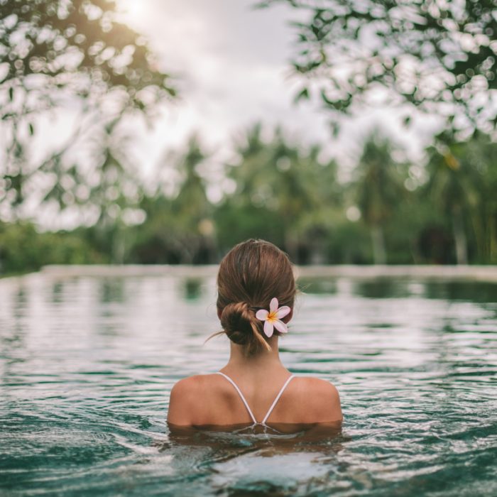 Frau entspannt sich in einem natürlichen Pool mit einer Blume im Haar, umgeben von Grün. Ideal für Ruhiger Rückzugsort Entdeckung.